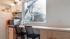 A kitchen with a window, two bar stools, a microwave, a coffee maker, and a refrigerator. - Designer E Austin Studio Close to Airport, Downtown, & UT Campus (Austin)