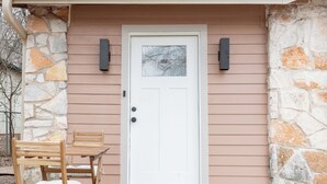 A white door with a glass panel, a stone wall, and a wooden table with chairs outside a building with wooden siding. - Designer E Austin Studio Close to Airport, Downtown, & UT Campus (Austin)