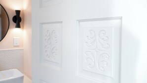 A bathroom with a white sink, wall-mounted light, and decorative paneling. - Designer E Austin Studio Close to Airport, Downtown, & UT Campus (Austin)
