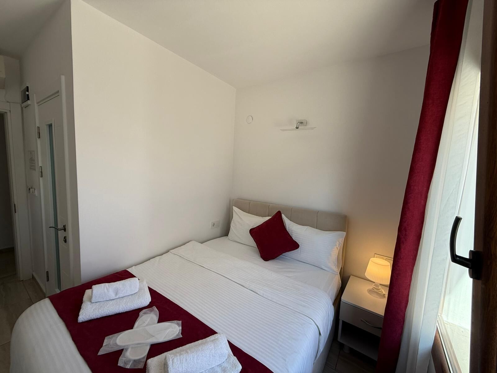 Quarto de hotel com cama, mesa de cabeceira, luminária e porta.
