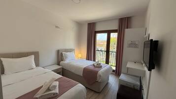 A hotel room with two beds, a TV, a desk, and a balcony with curtains.