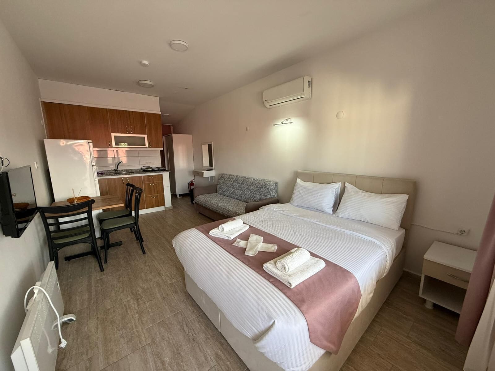 A hotel room with a bed, a sofa, a desk, and a kitchenette.