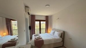 Hotelkamer met een bed, bureau met telefoon en afstandsbediening, spiegel en balkon met gordijnen.
