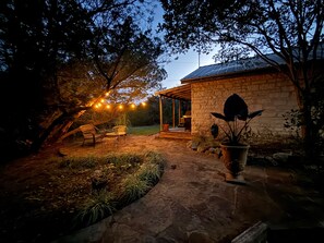 A stone patio with outdoor furniture, a potted plant, and string lights. - "Cheval Blanc" at Everwild Collective Cabins (Wimberley)