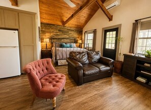 Ein gemütliches Wohnzimmer mit Kamin, einer braunen Ledersofa, einem rosa Sessel und einer Holzbalkendecke.