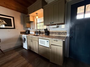 A kitchen with wooden cabinets, a built-in oven, a microwave, and a sink. - "Cheval Blanc" at Everwild Collective Cabins (Wimberley)
