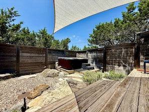 Eine Holzterrasse mit Whirlpool, umgeben von einem Holzzaun und Bäumen.