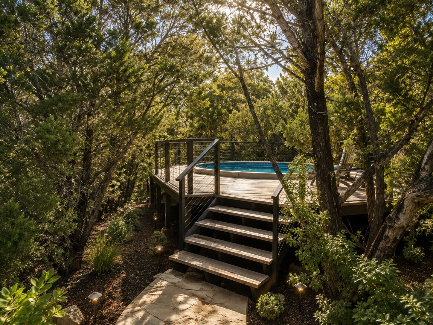 A wooden deck leading to a swimming pool surrounded by dense foliage.
