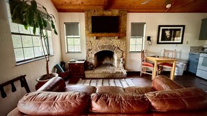 Ein Wohnzimmer mit Kamin aus Stein, einer Ledersofa und einer Holzbalkendecke, mit einem Fernseher darüber.