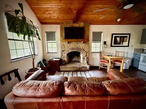 Ein Wohnzimmer mit Kamin aus Stein, einer Ledersofa und einer Holzbalkendecke, mit einem Fernseher darüber.