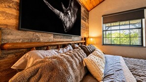 Ein Schlafzimmer mit einem hölzernen Kopfteil, einem großen Fenster und einem an der Wand befestigten Kunstwerk mit einem Dinosaurier.