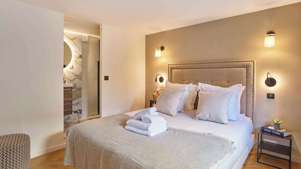 Une chambre à coucher avec un grand lit, une table de chevet sur laquelle se trouve un livre et une lampe fixée au mur.