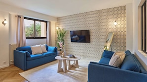 Un salon moderne avec un canapé bleu, une table basse, un téléviseur fixé au mur et un papier peint à motifs.