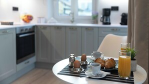 En frukostuppsättning med ägg, croissanter, kaffe och apelsinjuice på ett bord i ett modernt kök med vita skåp och ett fönster.