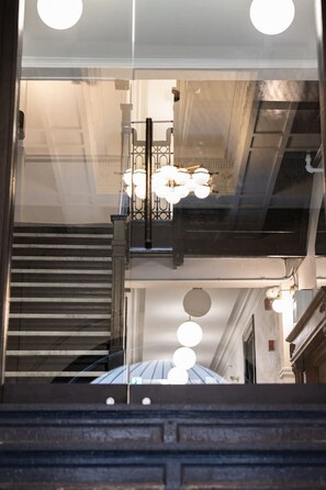 Un escalier avec une rampe en métal, un lustre et un plafond laissant apparaître les conduits.