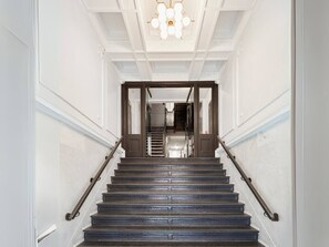 Un magnifique escalier, doté d’une rampe, menant à un palier surmonté d’un lustre.