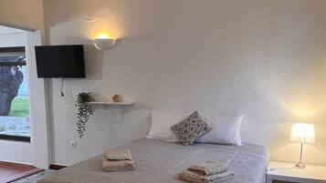 Un dormitorio con una cama, un televisor montado en la pared, una lámpara de noche y un estante pequeño con una planta.