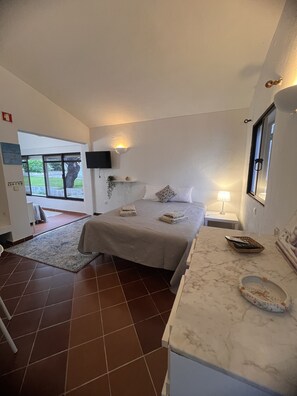 Une chambre à coucher avec un lit, une table de chevet, une lampe et une vue sur l’extérieur.