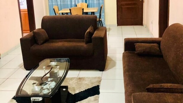 Un salón con un sofá marrón, una mesa de centro de vidrio y una alfombra estampada.