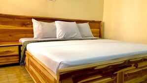 Una cama de madera con ropa de cama blanca en una habitación con cabecera de madera y una mesita de noche pequeña.