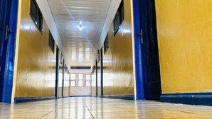 Un pasillo largo y estrecho con suelo de baldosas y puertas azules a ambos lados.