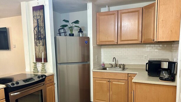 A kitchen with wooden cabinets, a stainless steel refrigerator, a stove, a sink, and a coffee maker.