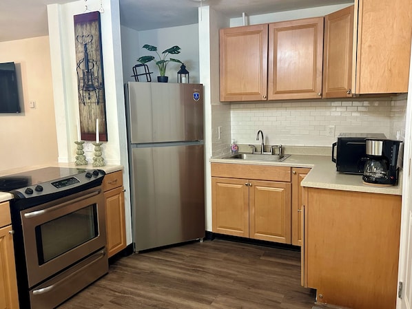 A kitchen with wooden cabinets, a stainless steel refrigerator, a stove, a sink, and a coffee maker.