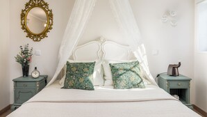 Een bed met hemelbed, twee nachtkastjes met decoratieve items, een spiegel aan de muur en een klok.