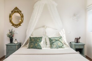 Ein Bett mit Baldachin, zwei Nachttische mit Dekoration, ein Wandspiegel und eine Uhr.