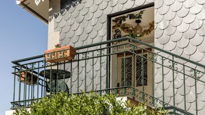 Een gebouw met een betegelde gevel, een balkon met ijzeren hekwerk en een raam met decoratieve luiken.