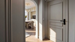 A hallway leading to a dining area with a round table and chairs, a kitchen in the background, and a white door with a black handle. - Modern, A/C Apartment - 2bdr/4p - Cannes/beach (Cannes)