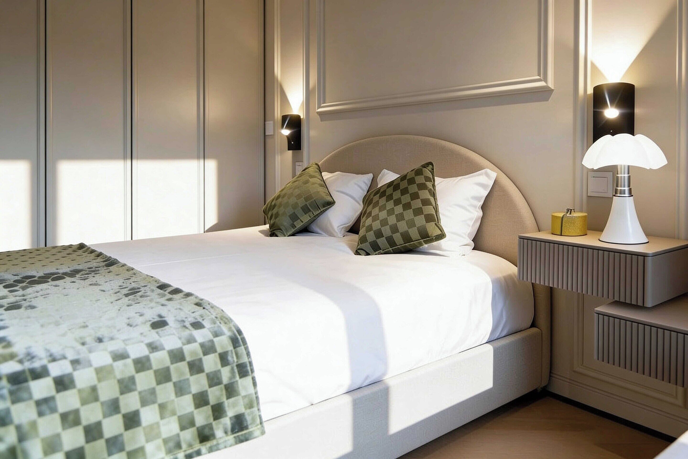 A neatly made bed with a checkered throw, two pillows, and a bedside lamp.