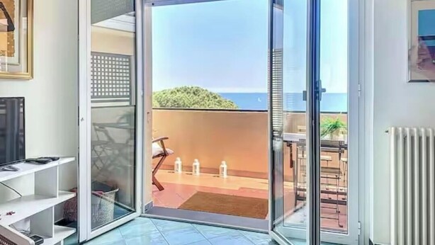 A room with a sliding glass door leading to a balcony with a view of the sea.