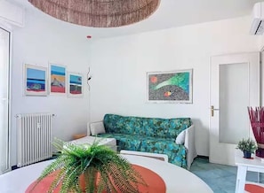 A room with a white radiator, a green sofa, a round table with a potted plant, and wall art. - Roses House - One Bedroom Apartment, Sleeps 2 (Arenzano)