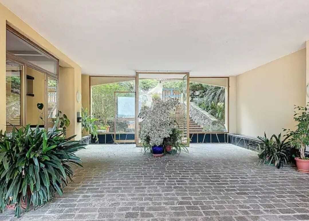 Un'area esterna riparata con pavimento in mattoni, piante in vaso e vista su una scala che conduce a un giardino.
