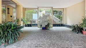 A covered outdoor area with a brick floor, potted plants, and a view of a staircase leading to a garden.