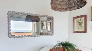 A room with a round white table, a potted plant, a mirror with a rope-like frame, and a hanging light fixture.