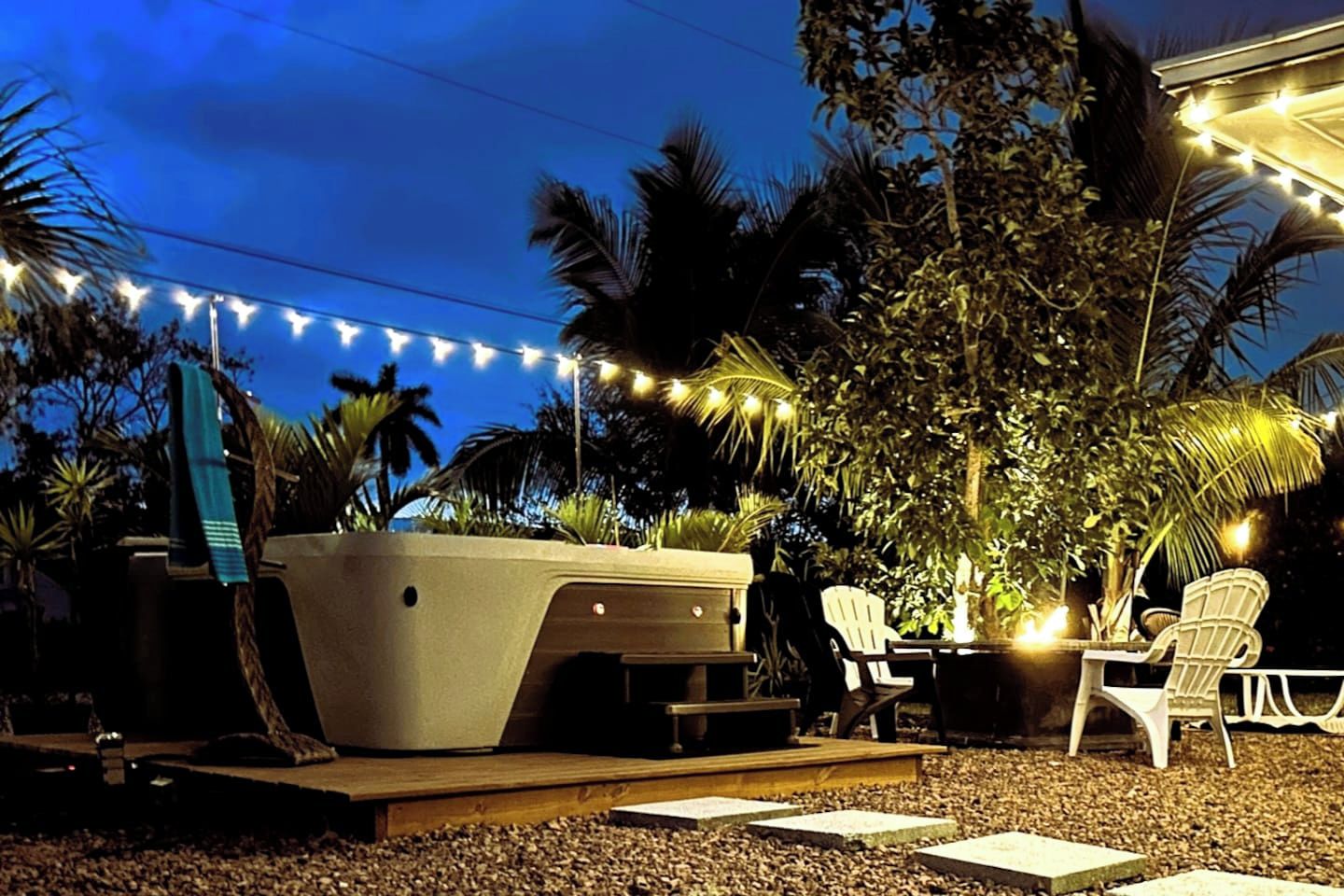 Un espacio al aire libre con hidromasaje, sillas blancas y guirnaldas de luces.