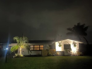 Ein zweistöckiges Haus mit einer gut beleuchteten Veranda und einem kleinen Garten.
