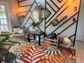 A modern living room with a geometric wall design, a patterned rug, a potted plant, a side table, and a bookshelf. - Coastal 2-bed Bungalow with Comfy King's, a Steamy Spa & AC in sunny Cape Coral (Cape Coral)