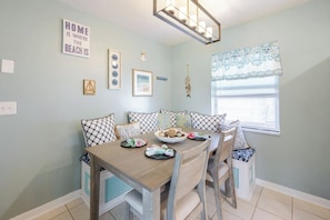 A dining area with a wooden table, checkered cushions, and a bowl of food. - Epic Relaxing Luxury Kings and Hot Tub Bungalow (Cape Coral)