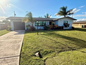 A residential house with a garage, a well-maintained lawn, and a clear sky. - Coastal 2-bed Bungalow with Comfy King's, a Steamy Spa & AC in sunny Cape Coral (Cape Coral)