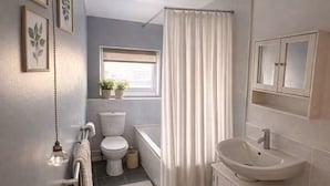 Et badeværelse med toilet, badekar, håndvask og et vindue med planter.