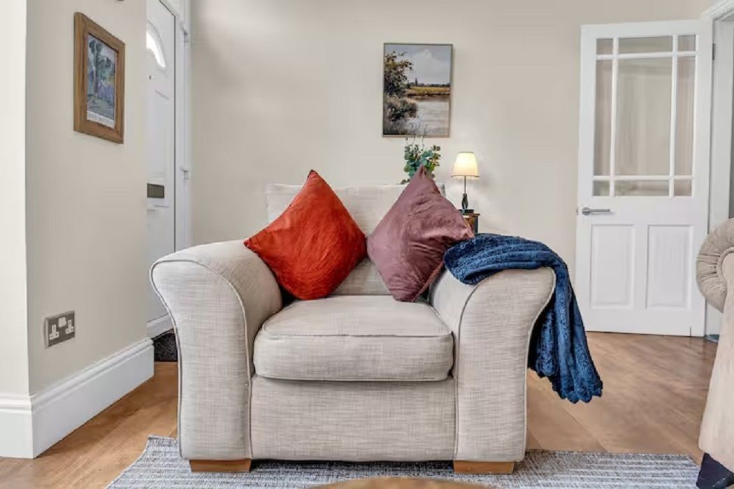 En stue med en beige sofa, to puder, en lampe og en dør.