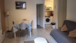 Een ruimtelijke leefruimte met een eethoek, een bank, een wasmachine en een keuken.