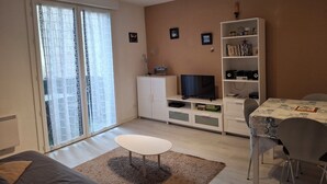 Een woonkamer met een televisie, boekenkast, eettafel en een bank.