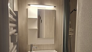 Een badkamer met een wit wastafelmeubel, spiegel en douche.