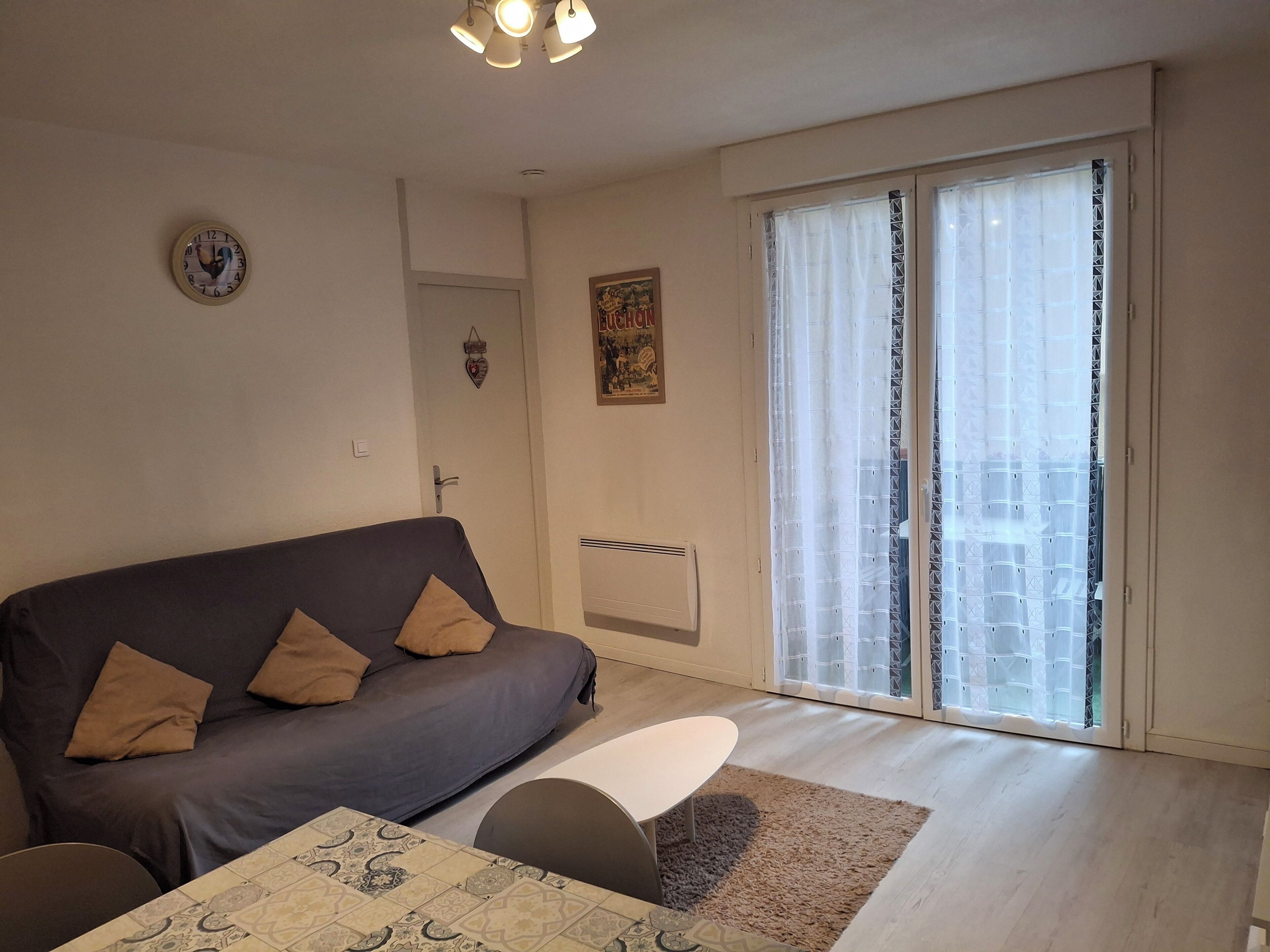 A living room with a sofa, a small table, a radiator, and a sliding glass door to the outside.