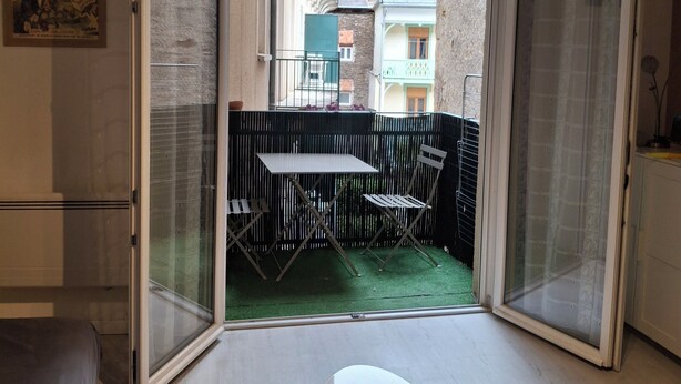 Een kamer met een schuifglasdeur die uitkomt op een buitenbalkon met een tafel en stoelen.