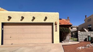 Un garaje residencial con una puerta color beige, un muro de piedra con una reja y un cielo azul despejado.
